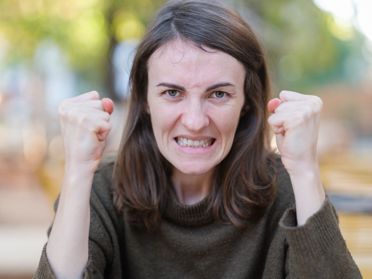 A young woman expressing anger with clenched fists in an outdoor setting during fall.